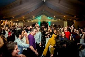A crowd of people dancing and celebrating inside a dimly lit event tent.