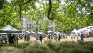 People gather on an outdoor area surrounded by trees and event tents.