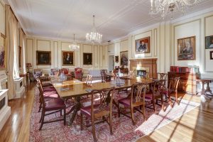 A formal meeting room arranged with tables in a U-shape, featuring a fireplace, traditional artwork, and ornate chandeliers.