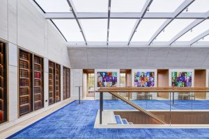 Inner Temple library interior featuring tall bookshelves, colourful pop art portraits, blue carpet, and glass railing staircase.